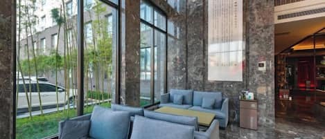 A modern lobby with large windows, grey sofas, and a stone wall with a vertical text display.