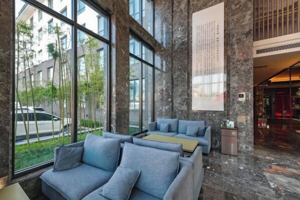 A modern lobby with large windows, grey sofas, and a stone wall with a vertical text display. - Zhouchun Hotel (Zibo)