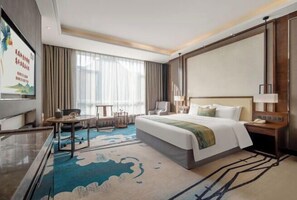 A hotel room with a large bed, a desk with a chair, a TV, and a large window with curtains. - Zhouchun Hotel (Zibo)