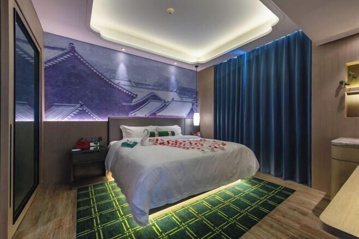 A hotel room with a bed, a nightstand, a wall-mounted TV, and a large window with curtains.