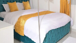 Un dormitorio con cabecera capitonada color turquesa, cama con dosel blanco y manta decorativa amarilla.