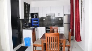 Una cocina compacta con armarios blancos, salpicadero de azulejos negros y un taburete azul.