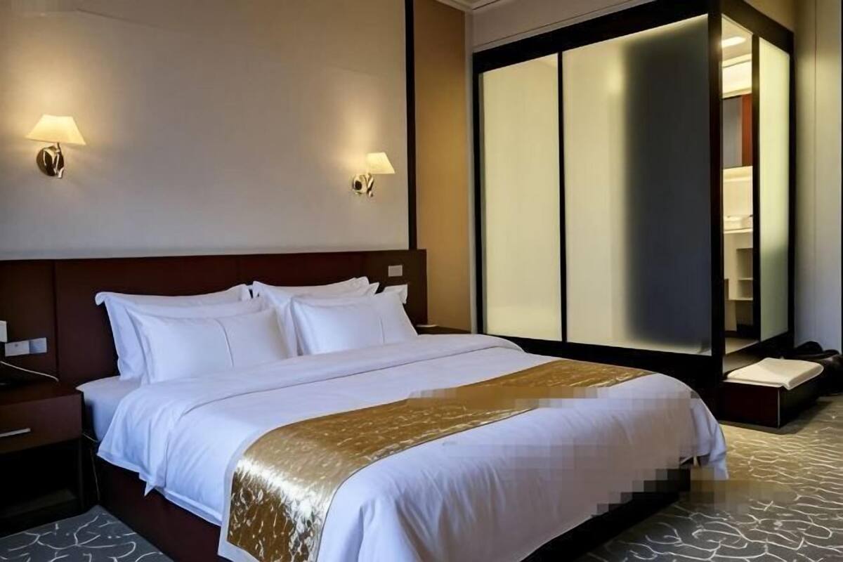 A hotel room with a large bed, bedside tables, a wardrobe, and wall-mounted lamps.