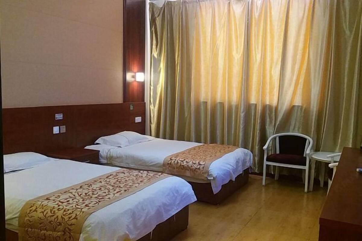 A hotel room with two beds, a chair, a desk, and a curtain.
