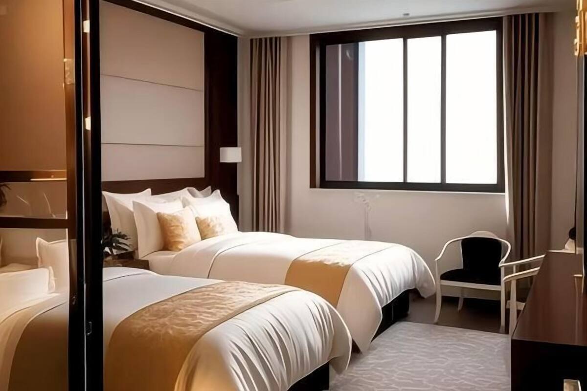 A hotel room with two beds, a desk, a chair, a large window, and a wardrobe.