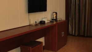 A hotel room with a wooden desk, a flat-screen TV mounted on the wall, a kettle, and a coffee maker.