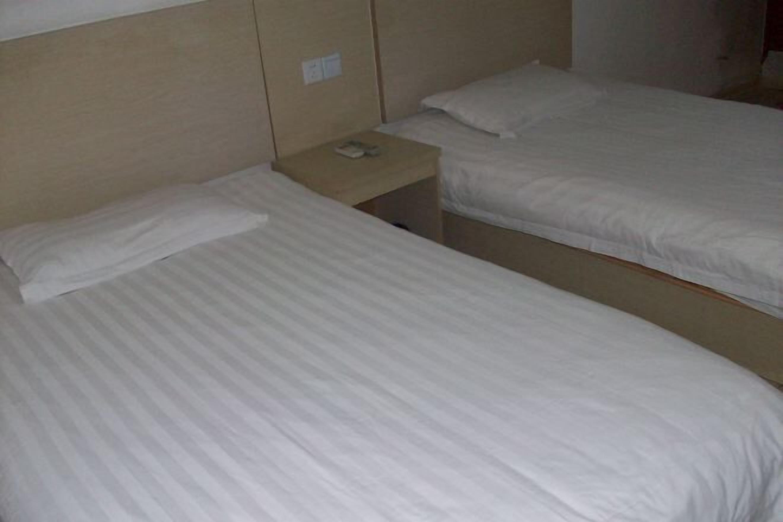 A hotel room with two single beds, each with a wooden headboard and a small bedside table with a phone.