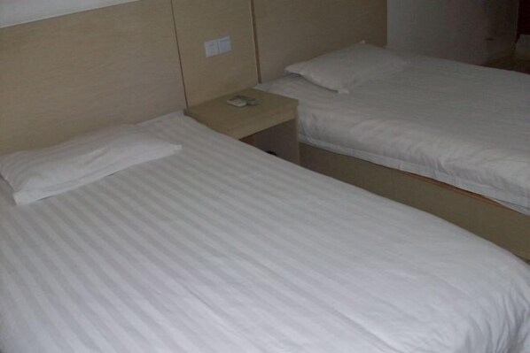 Een hotelkamer met twee eenpersoonsbedden, elk met een houten hoofdbord en een klein nachtkastje met een telefoon.