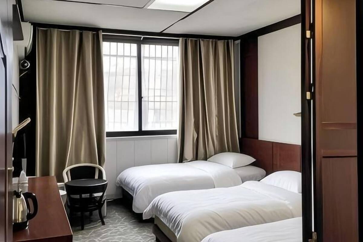 A hotel room with two beds, a desk, a chair, and a window with curtains.