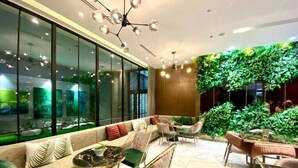 A modern lounge area with seating, a glass wall, and a green wall with plants. - Zenity Apartment Quan 1 (Ho Chi Minh City)