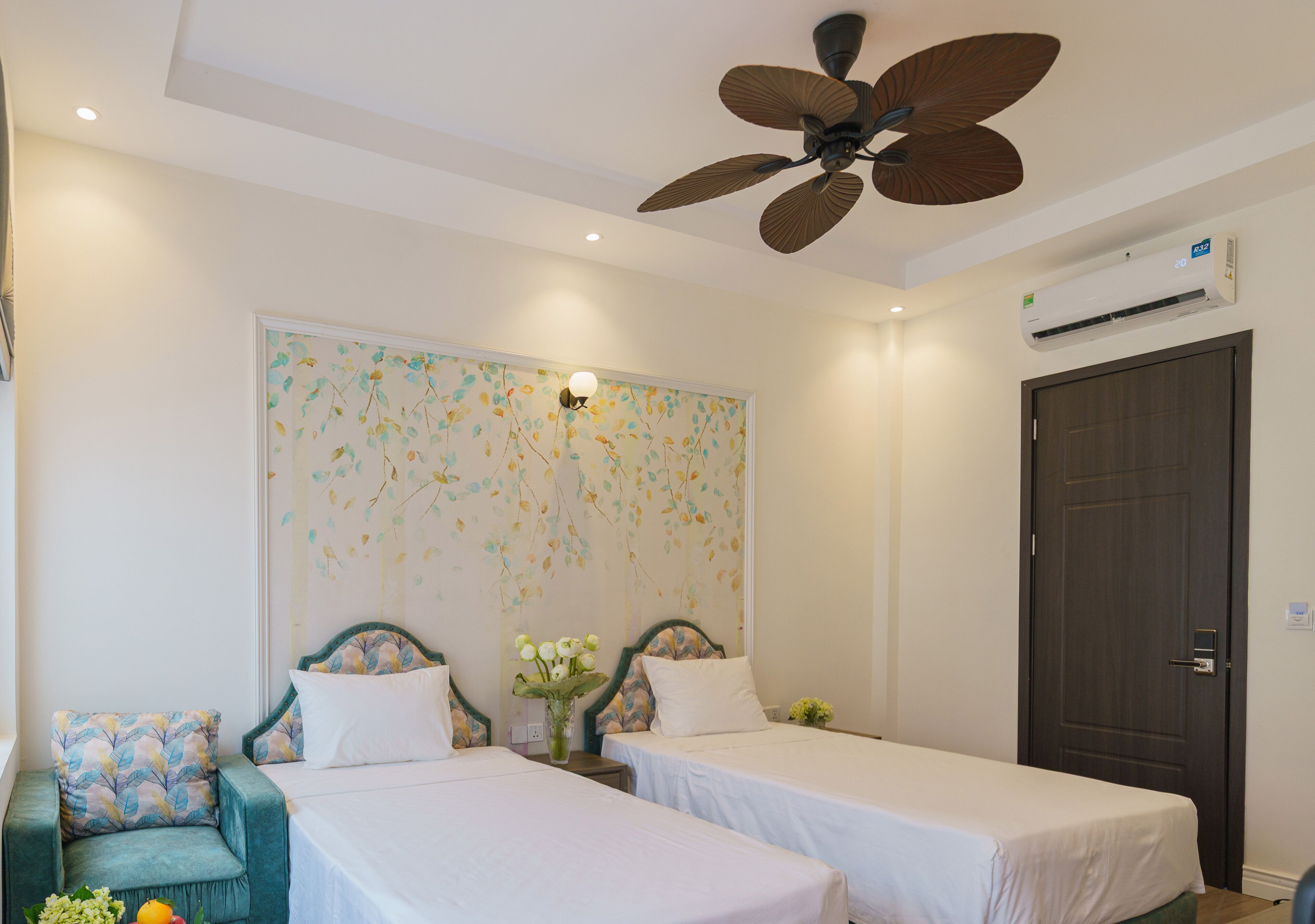 A hotel room with two single beds, a ceiling fan, an air conditioning unit, a decorative wall, and a door.