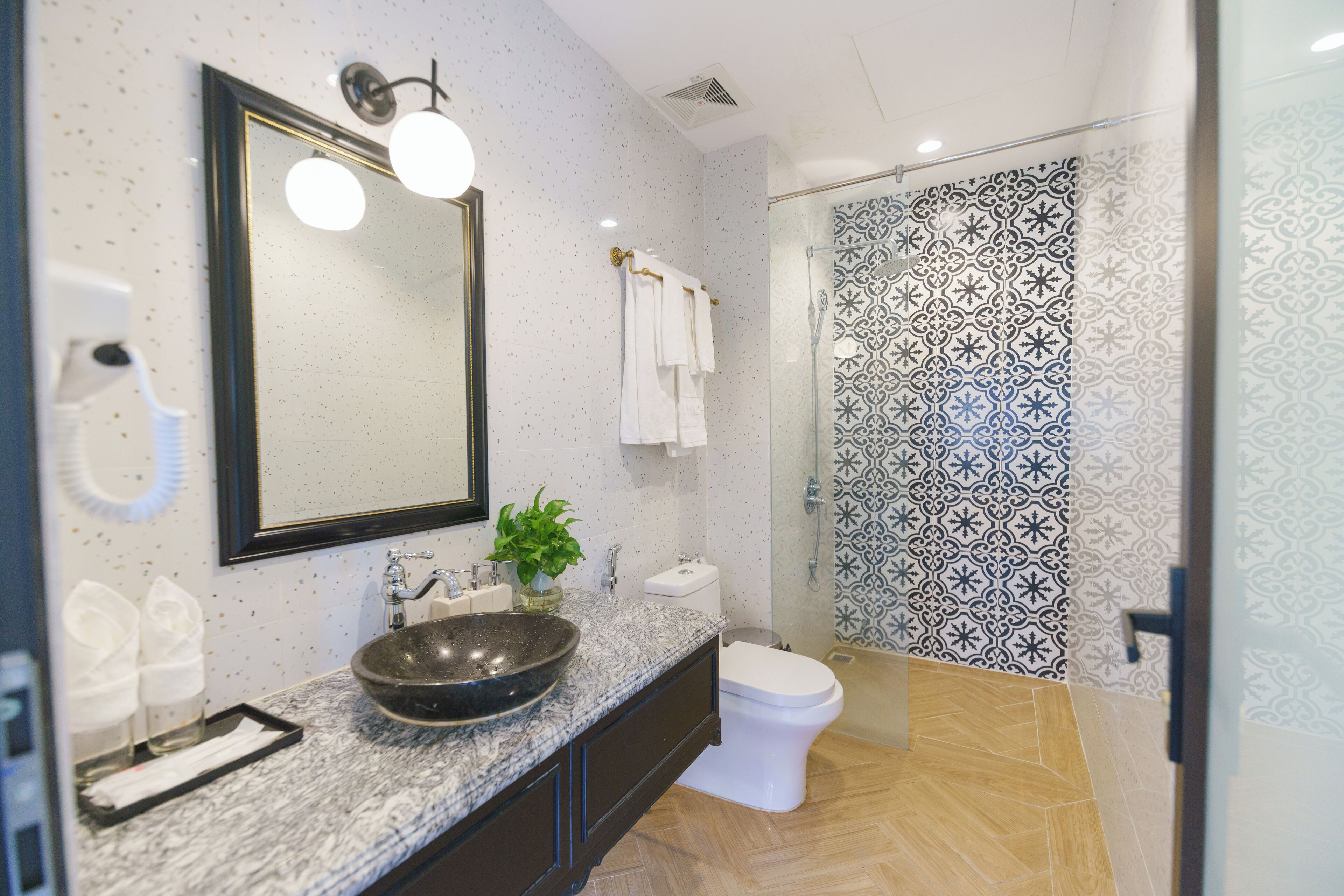 A modern bathroom with a large mirror, a sink with a bowl, a toilet, and a shower with patterned tiles.
