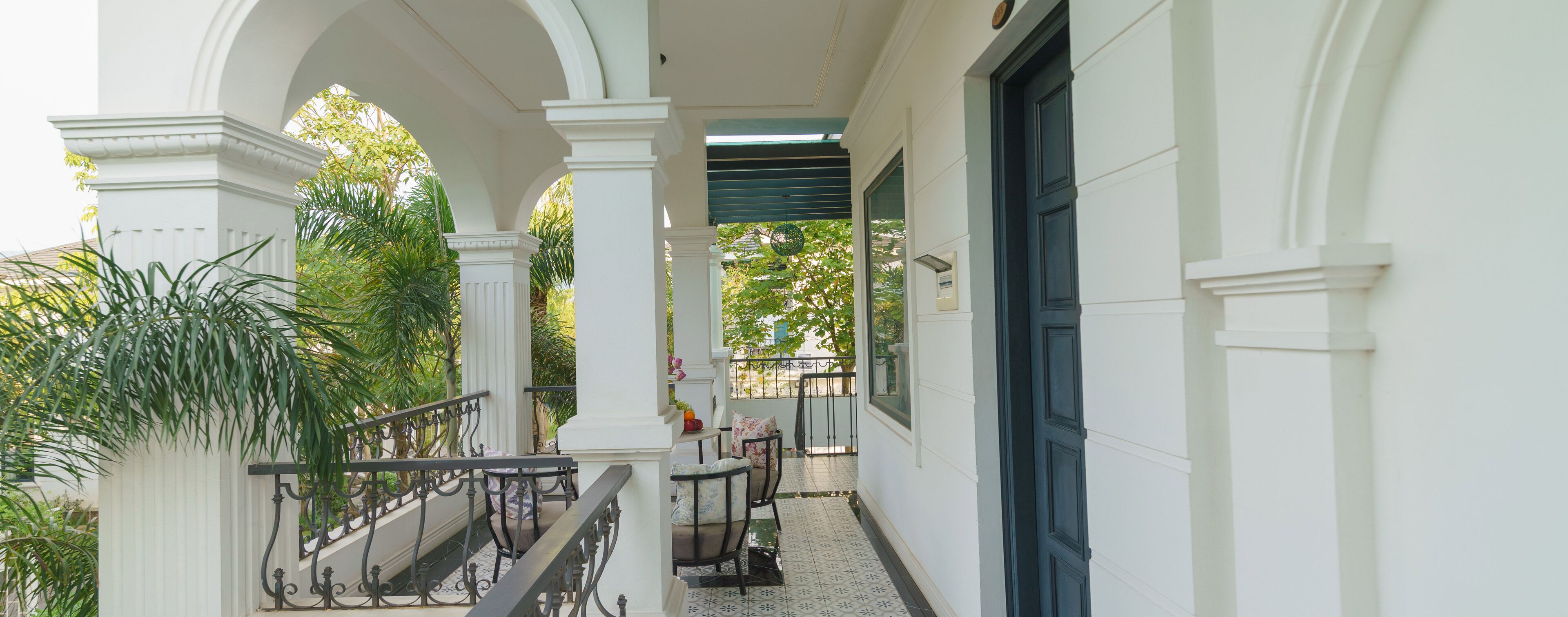 Varanda coberta com guarda-corrimão branco, soalho em azulejos e vista para o verde lá fora.