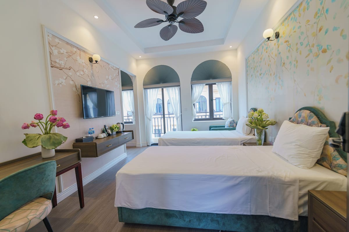 A bedroom with a bed, a desk, a chair, a TV, and a ceiling fan.
