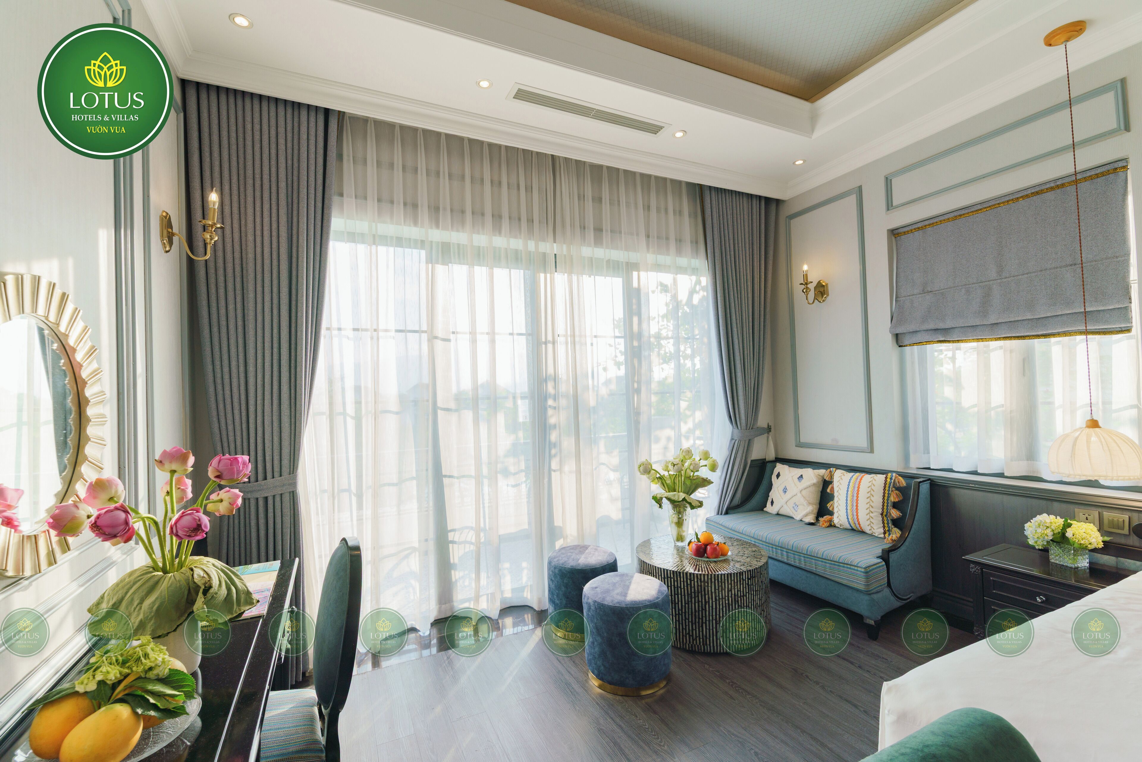 Una habitación de hotel con un ventanal grande, un sofá, una mesa de comedor con sillas y un jarrón decorativo con flores.
