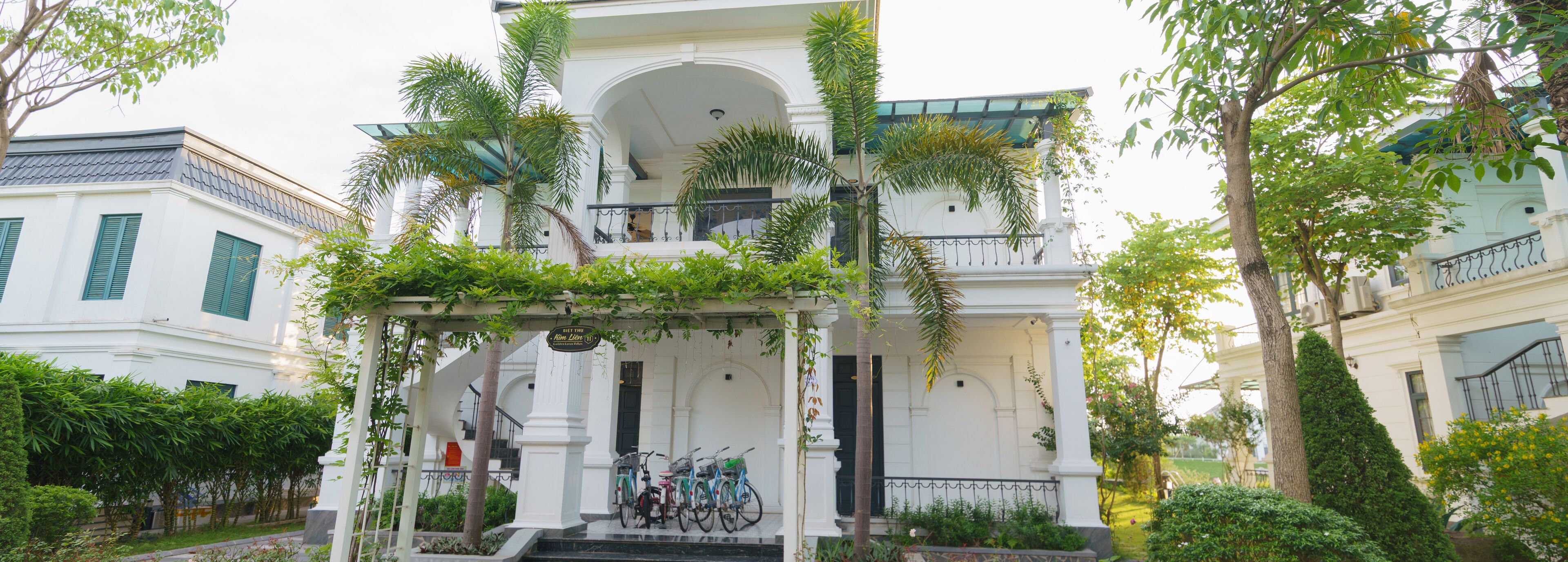 A white building with a covered porch, a staircase, and bicycles parked in front.
