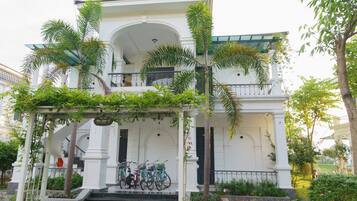 A white building with a covered porch, a staircase, and bicycles parked in front.
