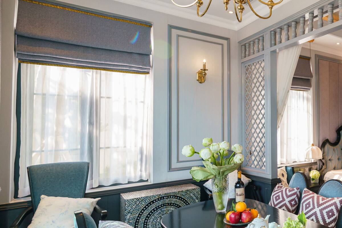 A hotel room with a bed, a dining table with fruit and a vase, a chair, and a decorative wall panel.