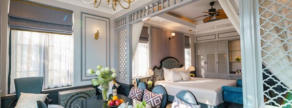 A hotel room with a bed, a dining table with fruit and a vase, a chair, and a decorative wall panel. - Lotus Hotel - Vuon vua (Thanh Thuy)