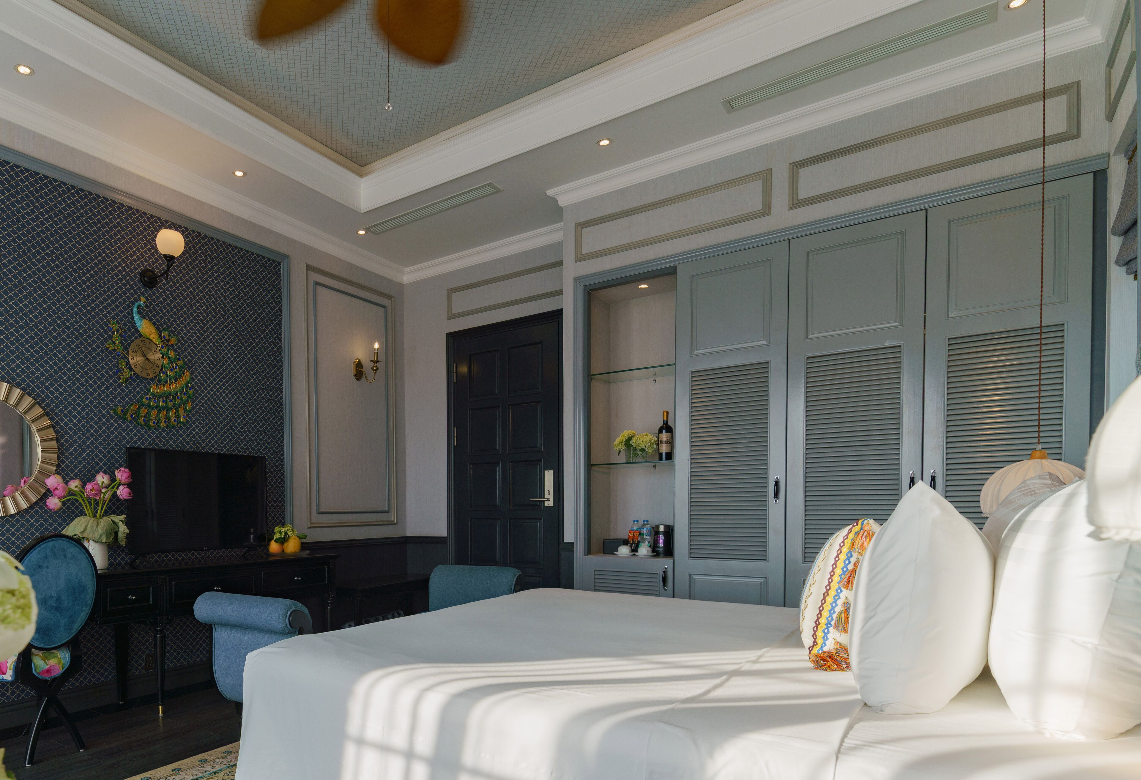 A hotel room with a large bed, a desk with a TV, a wardrobe, and a decorative wall.