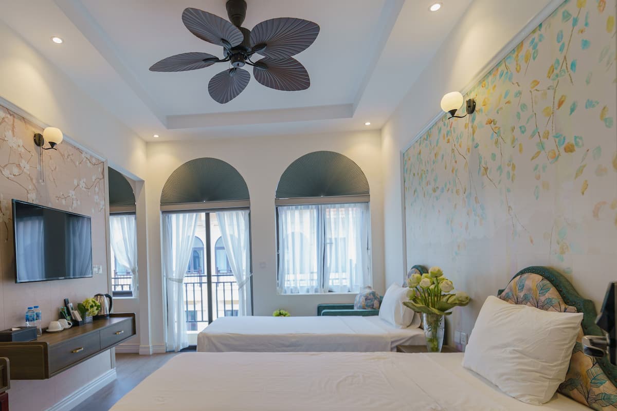 A hotel room with two beds, a ceiling fan, a TV, and a balcony with a view.