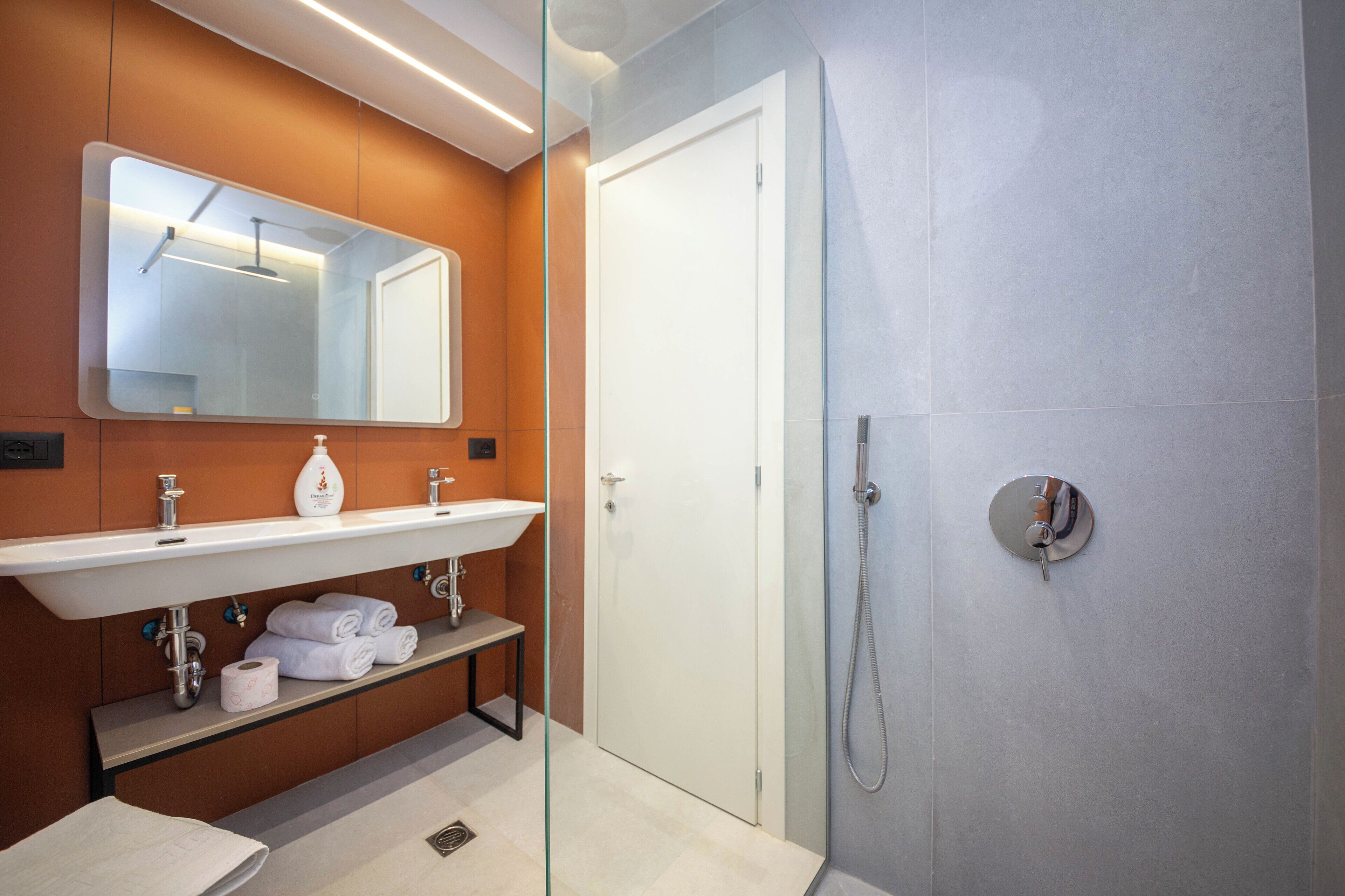 Un baño moderno con cabina de ducha de vidrio, un lavabo blanco con espejo y un estante con toallas y artículos de aseo.