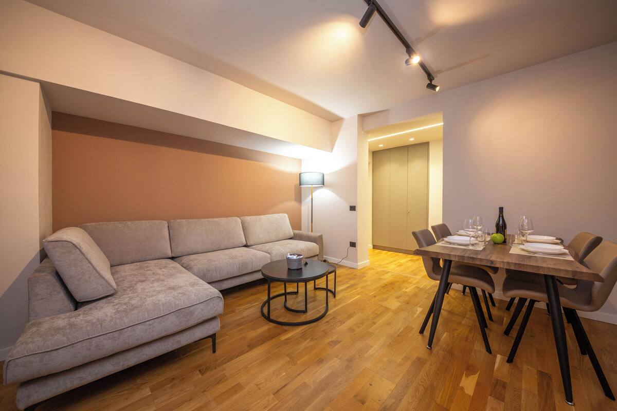 A modern living room with a sectional sofa, a round coffee table, and a dining table set for four.