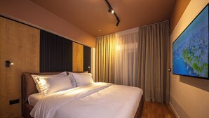 A modern bedroom with a large bed, wooden paneling on one wall, a large window with curtains, and a flat-screen TV mounted on the wall. - Blloku Unique Apartments 2 (Tirana)