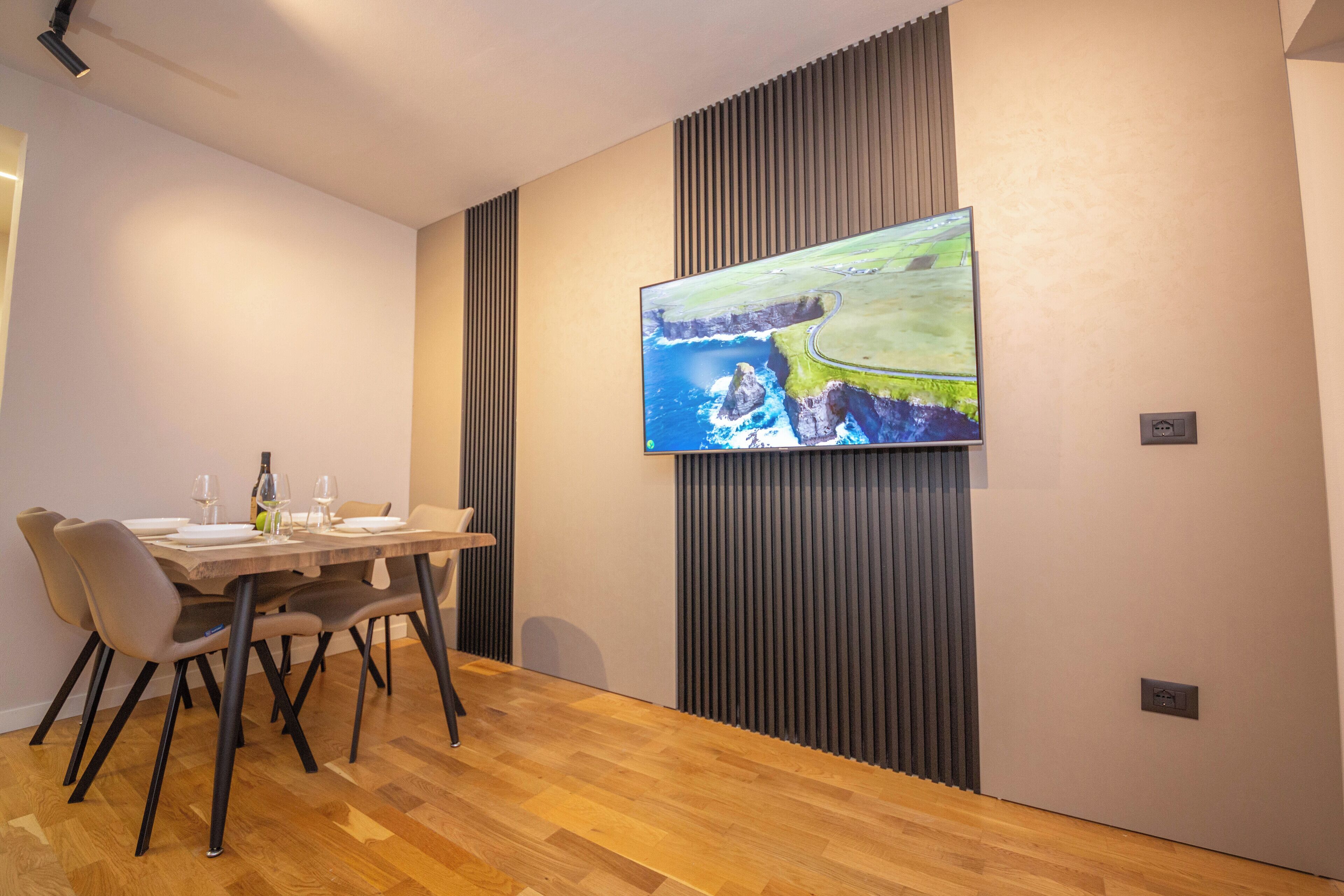 Un comedor con una mesa de madera, sillas y un cuadro de un paisaje costero.