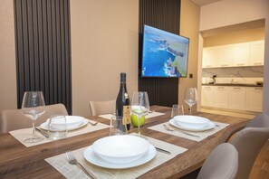A dining table set with plates, glasses, and a bottle, with a TV mounted on the wall displaying a scenic view. - Blloku Unique Apartments 2 (Tirana)