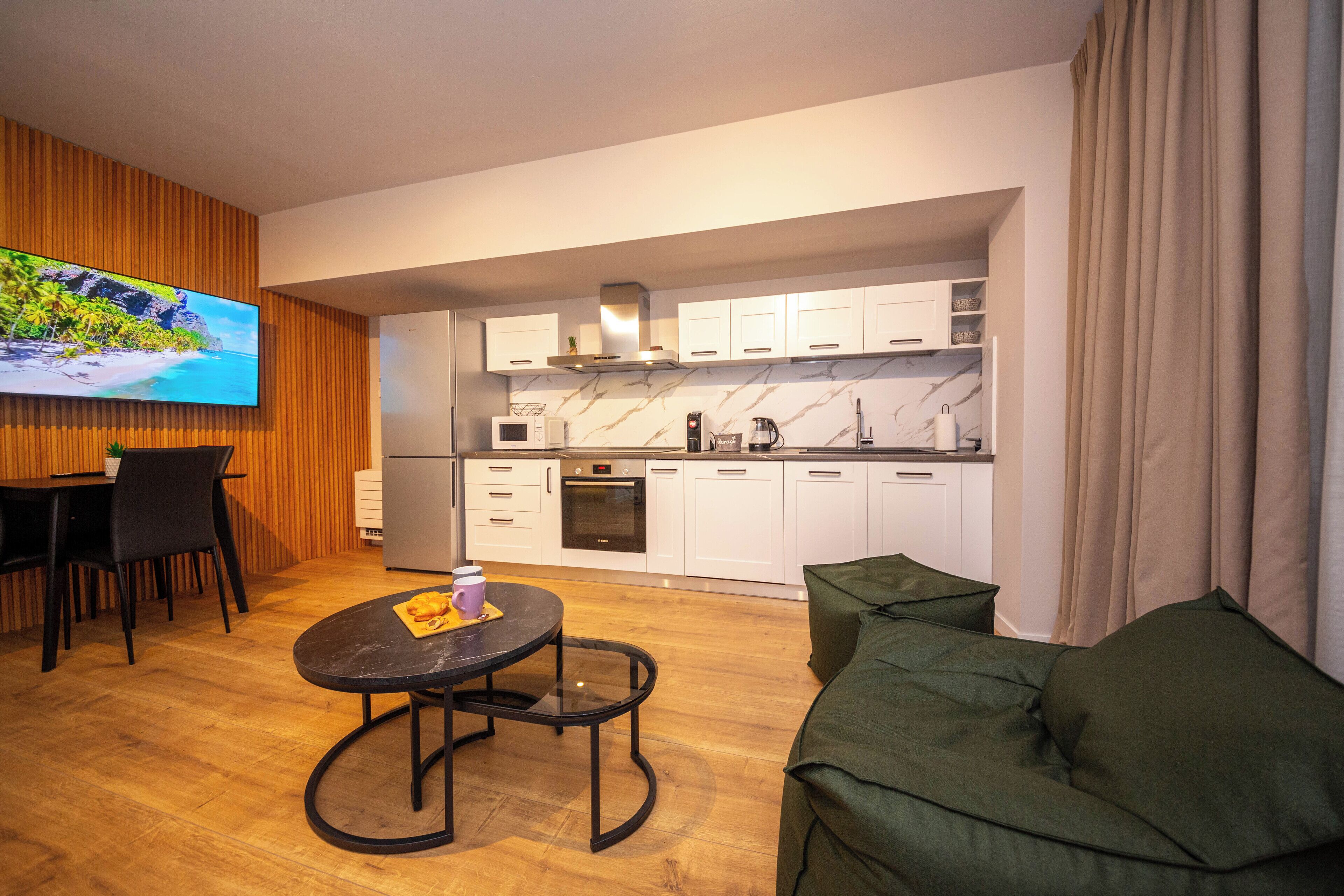 A modern kitchen with white cabinets, a built-in oven, and a large flat-screen TV mounted on a wooden wall.