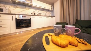 A modern kitchen with white cabinets, a marble countertop, and a wooden table with croissants and coffee mugs. - Blloku Unique Apartments 2 (Tirana)