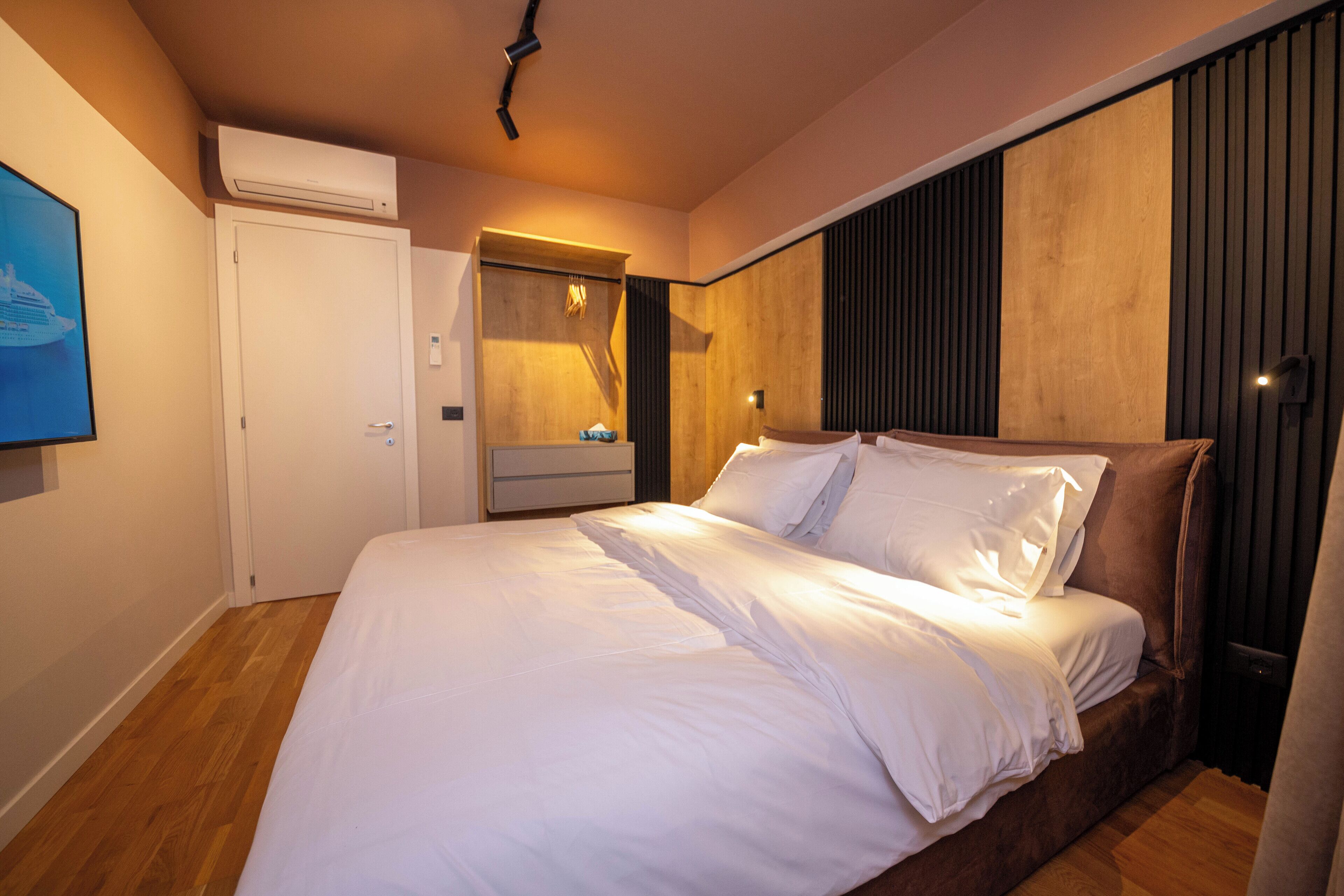 Une chambre avec un grand lit, un plancher en bois, une porte blanche et un climatiseur fixé au mur.