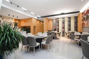 A modern dining area with round tables and chairs, a large potted plant, and a menu board. - Huangguoshu Sunflower Hotel (Zhenning)