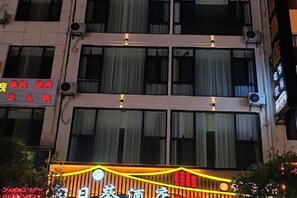 Fachada de hotel con múltiples ventanas, algunas con cortinas. Se observan carteles que indican los tipos de habitación y precios.