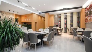 Un restaurante moderno con mesas y sillas redondas, una planta grande en maceta y una pizarra de menú.