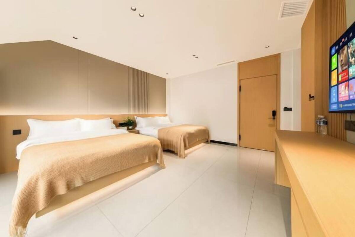 A modern hotel room with two beds, a wooden headboard, a flat-screen TV, and a reception desk.
