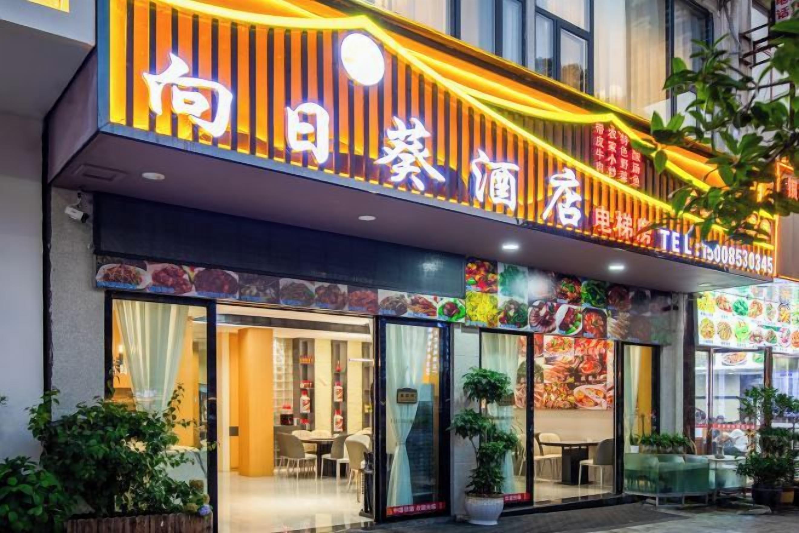 A restaurant with a brightly lit sign, large windows, and outdoor seating.