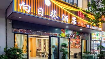 A restaurant with a brightly lit sign, large windows, and outdoor seating.