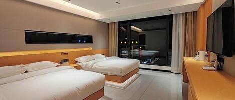 A modern hotel room with two beds, a flat-screen TV mounted on the wall, a desk with a lamp, and a large window with curtains.