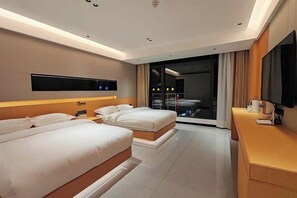 Una habitación de hotel moderna con dos camas, un televisor de pantalla plana montado en la pared, un escritorio con una lámpara y un ventanal con cortinas.