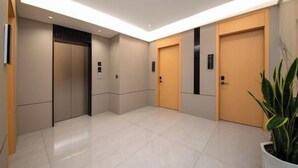 Un área de ascensores moderna con dos ascensores, una planta en maceta y un piso de baldosas limpias.