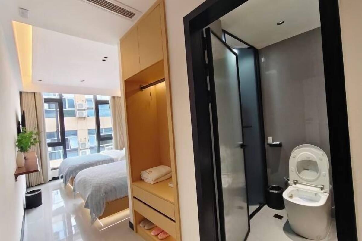A modern hotel room with a large bed, a small seating area, and a separate bathroom with a toilet and sink.