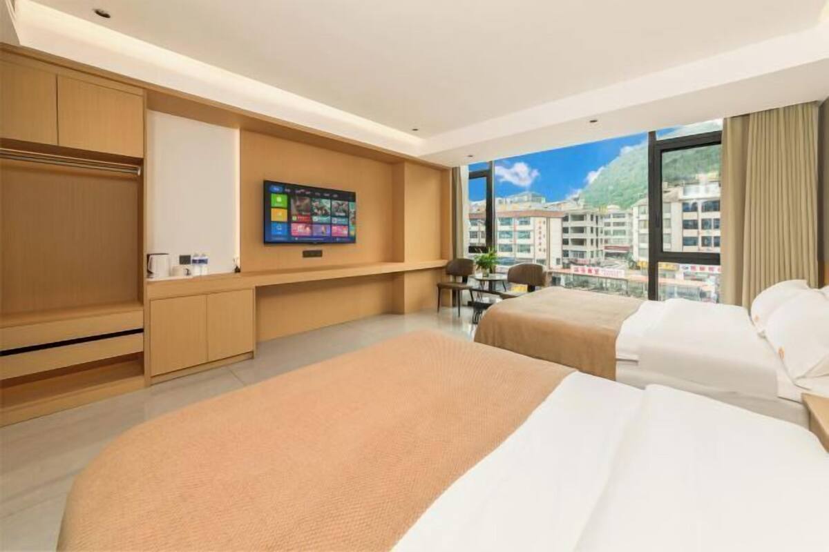 A hotel room with two beds, a desk, a TV, and a city view.