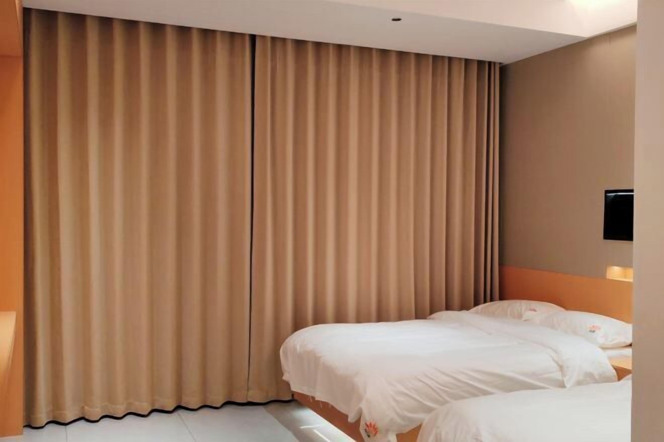 A hotel room with two beds, beige curtains, and a wall-mounted TV.
