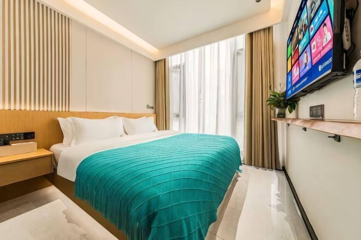 A modern hotel room with a large bed, a flat-screen TV, a bedside table, and a large window.