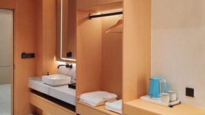 Un baño moderno con tocador de madera, un espejo grande y una cafetera sobre la encimera.