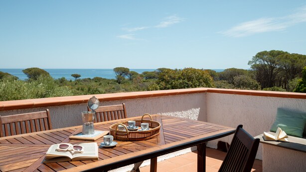 A wooden table with a book, sunglasses, and a tea set on a balcony overlooking the sea. - Casa dell'Asfodelo by Wonderful Italy (Budoni)