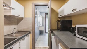 A narrow kitchen with a sink, stove, and microwave. A door leads to a bathroom. - Ursino apartment with balcony by Wonderful Italy (Catania)