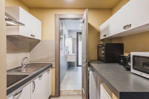 Cocina estrecha con pileta, estufa y microondas. Una puerta da a un baño.
